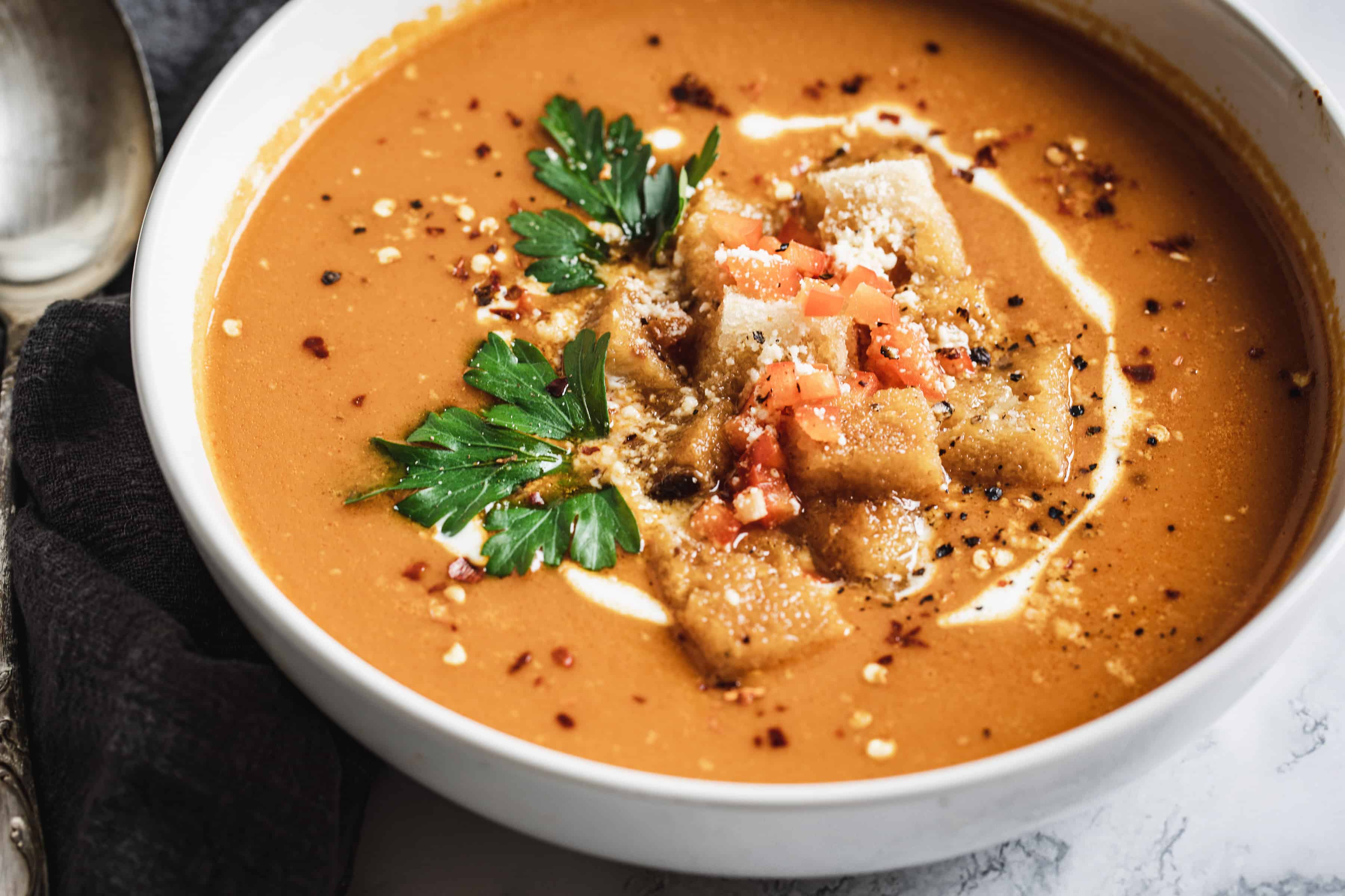 Bell pepper soup in white bowl with croutons and herbs.