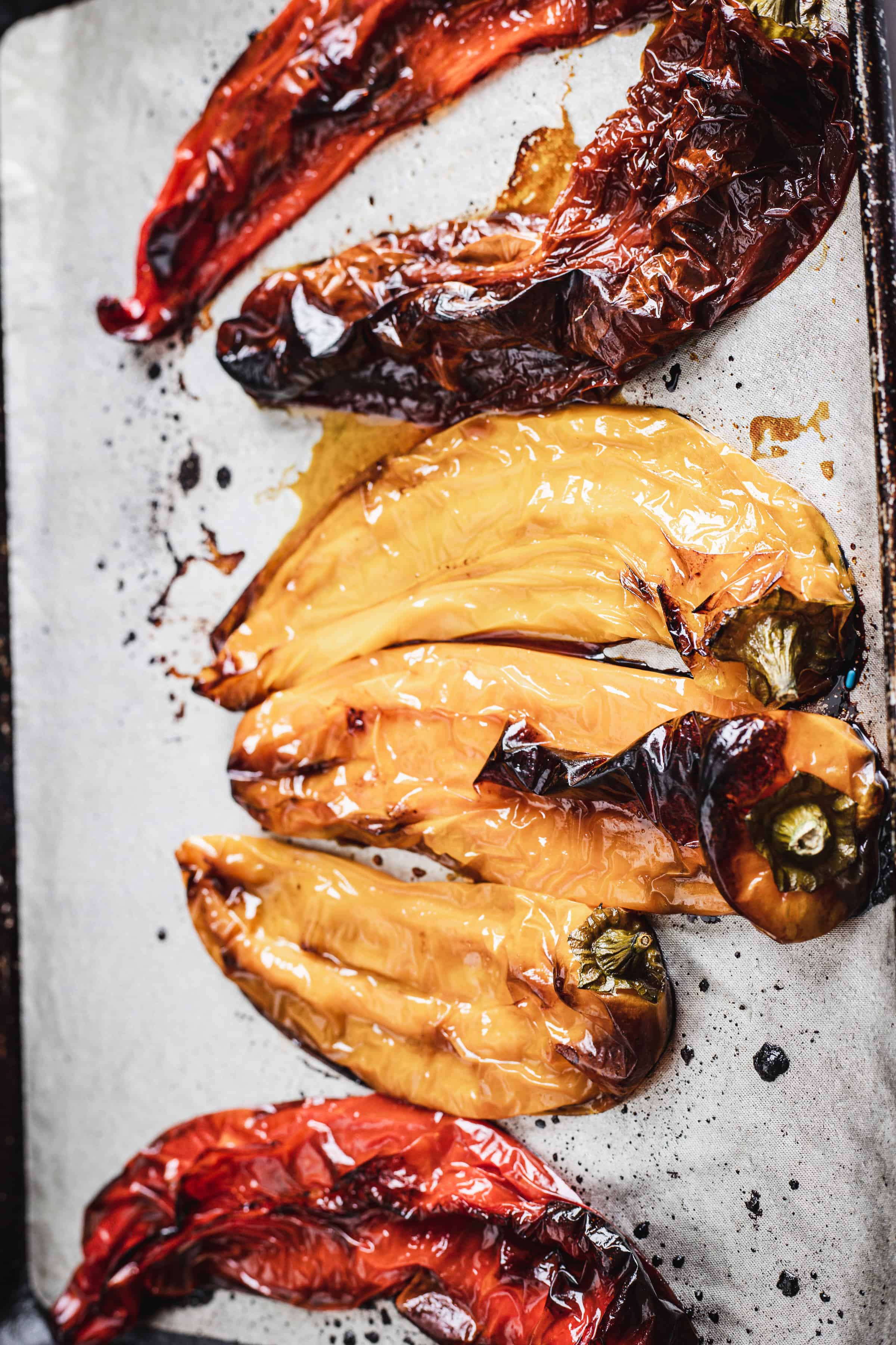 Roasted bell peppers in red and yellow colors, perfect for a rich bell pepper bisque, showing charred and wrinkled skins on a metal baking sheet.
