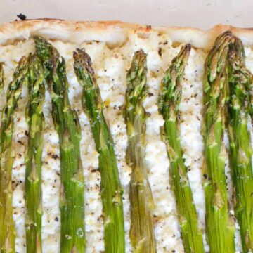 A rectangular asparagus tart is shown. The tart has a light, flaky crust and is topped with a creamy cheese layer. It is garnished with whole asparagus spears arranged neatly in rows across the top. Ideal for quick recipes, the tart appears freshly baked with visible brown edges.