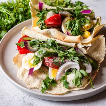 A plate of fresh salad with various vegetables and herbs from Grandma's Recipes, served on pieces of pita bread.
