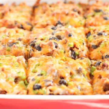 A casserole dish filled with enchiladas topped with melted cheese and black beans, freshly baked and served hot.