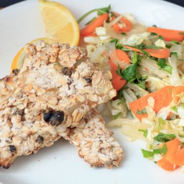 A plate with a piece of grilled fish and a side of carrot and cabbage slaw, garnished with a lemon wedge. the dish is presented on a wooden table.