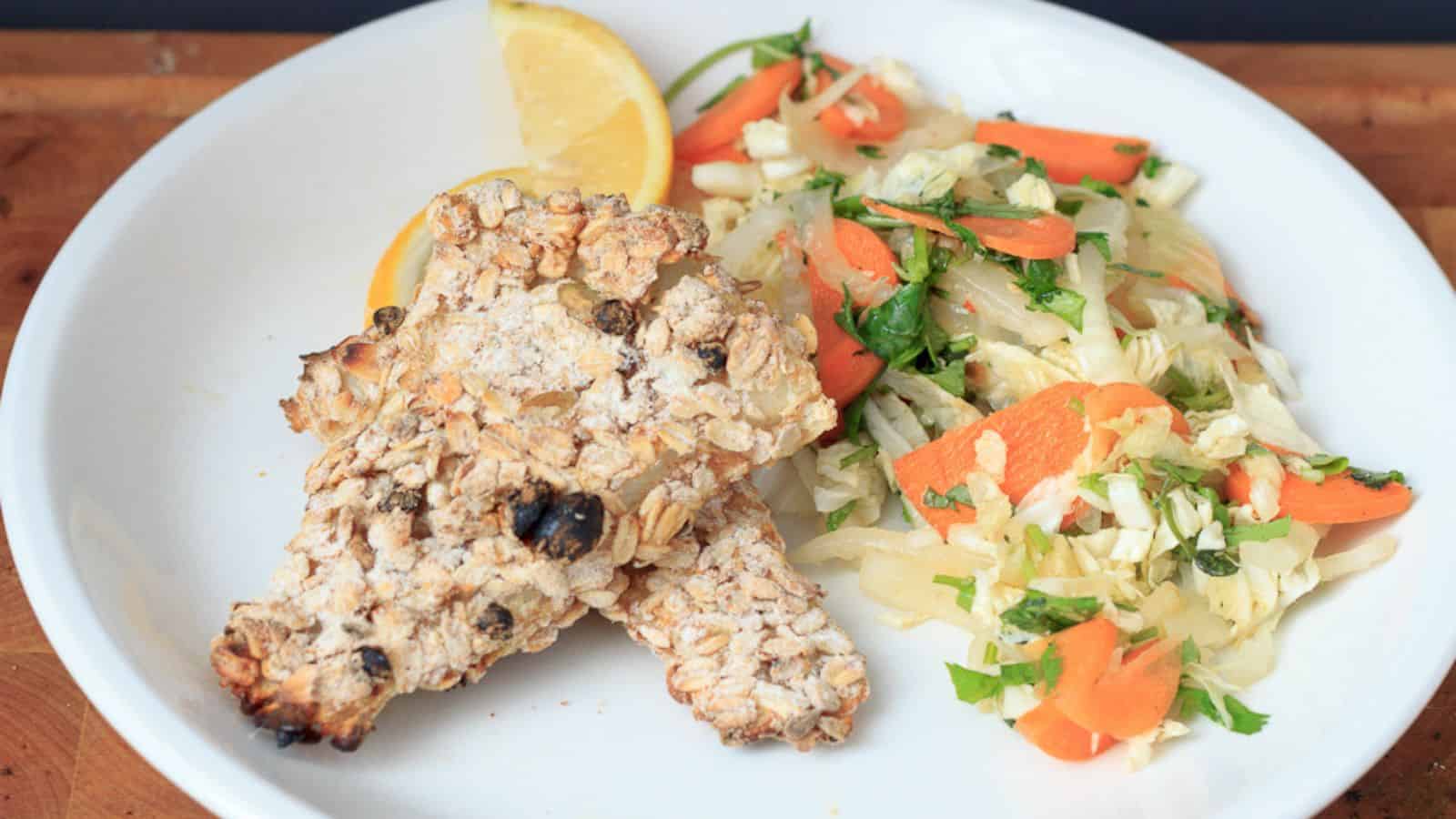 A plate with a piece of grilled fish and a side of carrot and cabbage slaw, garnished with a lemon wedge. the dish is presented on a wooden table.