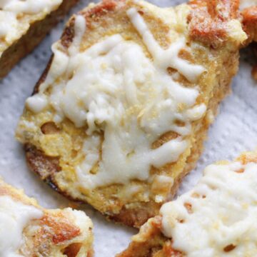 Close-up view of golden brown French toast slices topped with melted cheese, arranged on a white paper towel. The surface of the toast appears slightly crispy, and the melted cheese is spread unevenly across the pieces. This cheap recipe from Grandpa's collection will have you begging for more.
