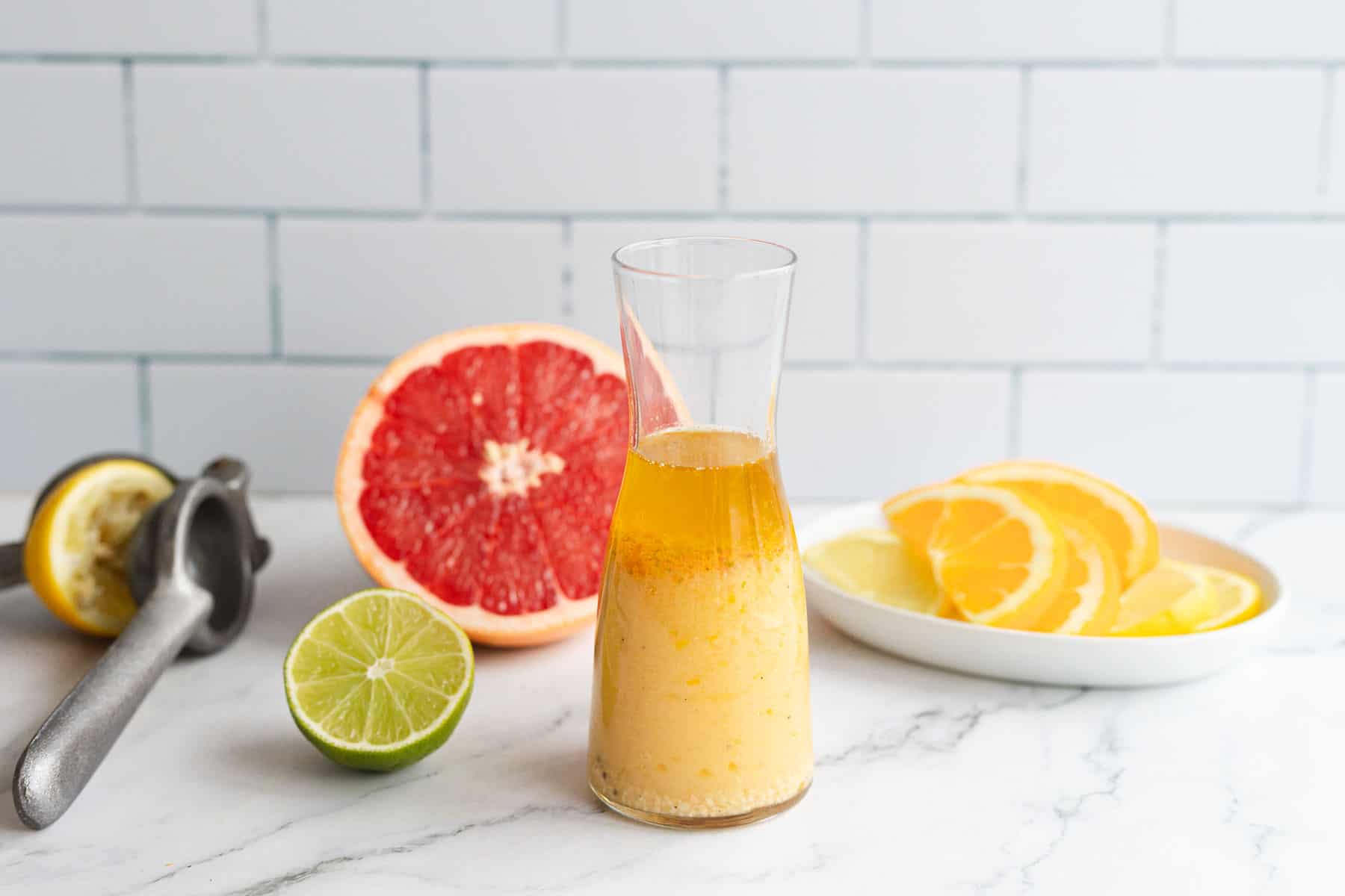 A glass bottle with a citrus marinade, sits next to a plate of fruit.