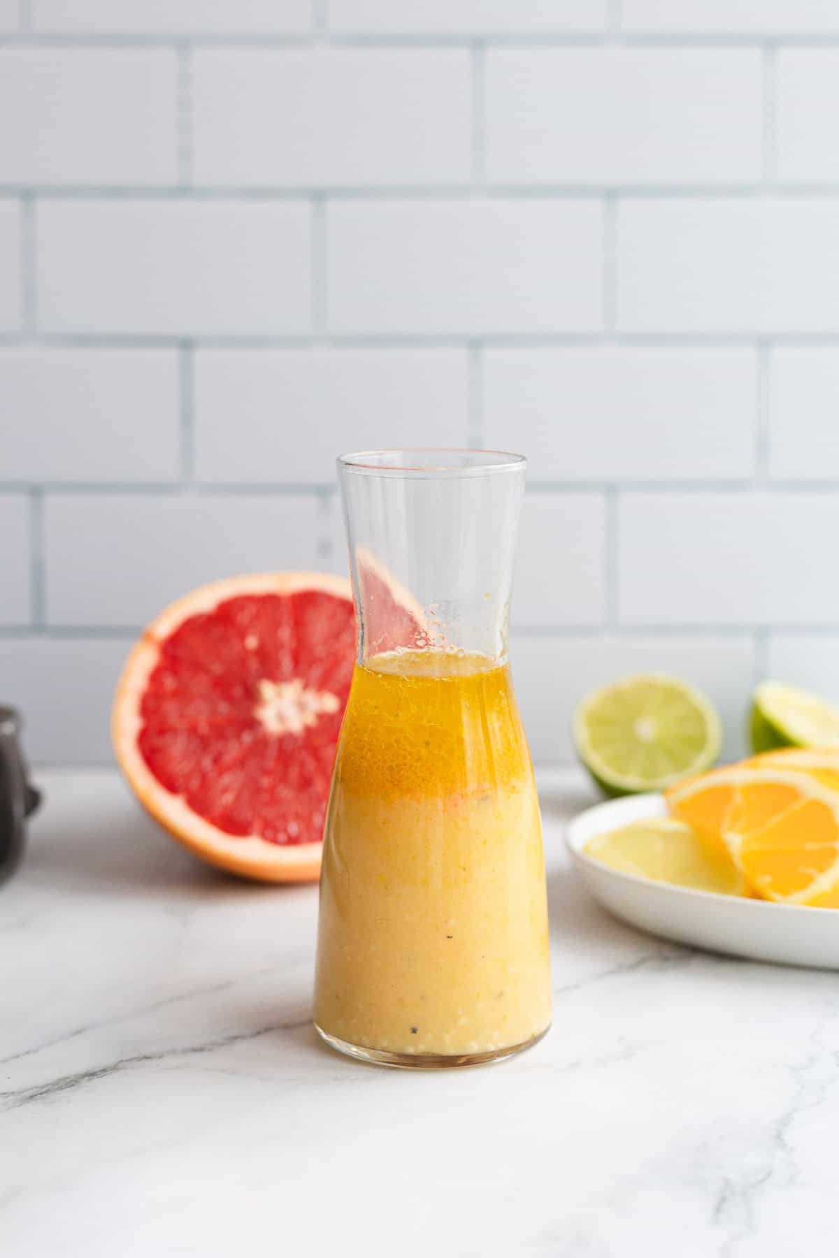 A glass bottle with a citrus marinade, sits next to a plate of fruit.