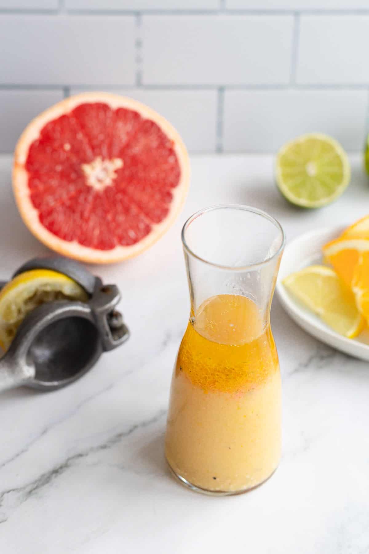 A glass bottle with a citrus marinade, sits next to a plate of fruit.