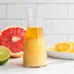 A glass bottle with a citrus marinade, sits next to a plate of fruit.