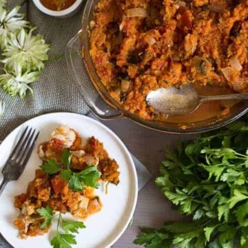 A plate of food on a table next to a bowl of parsley.