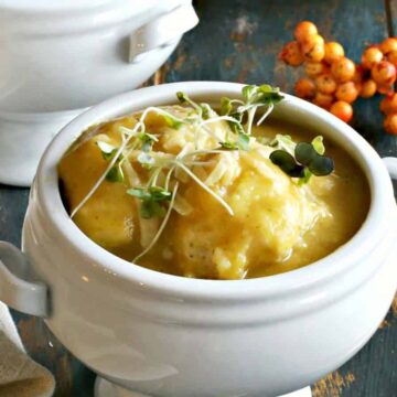 A bowl of creamy potato soup garnished with sprouts, served on a rustic wooden table accompanied by a white soup tureen and a golden spoon, inspired by 1960s recipes.