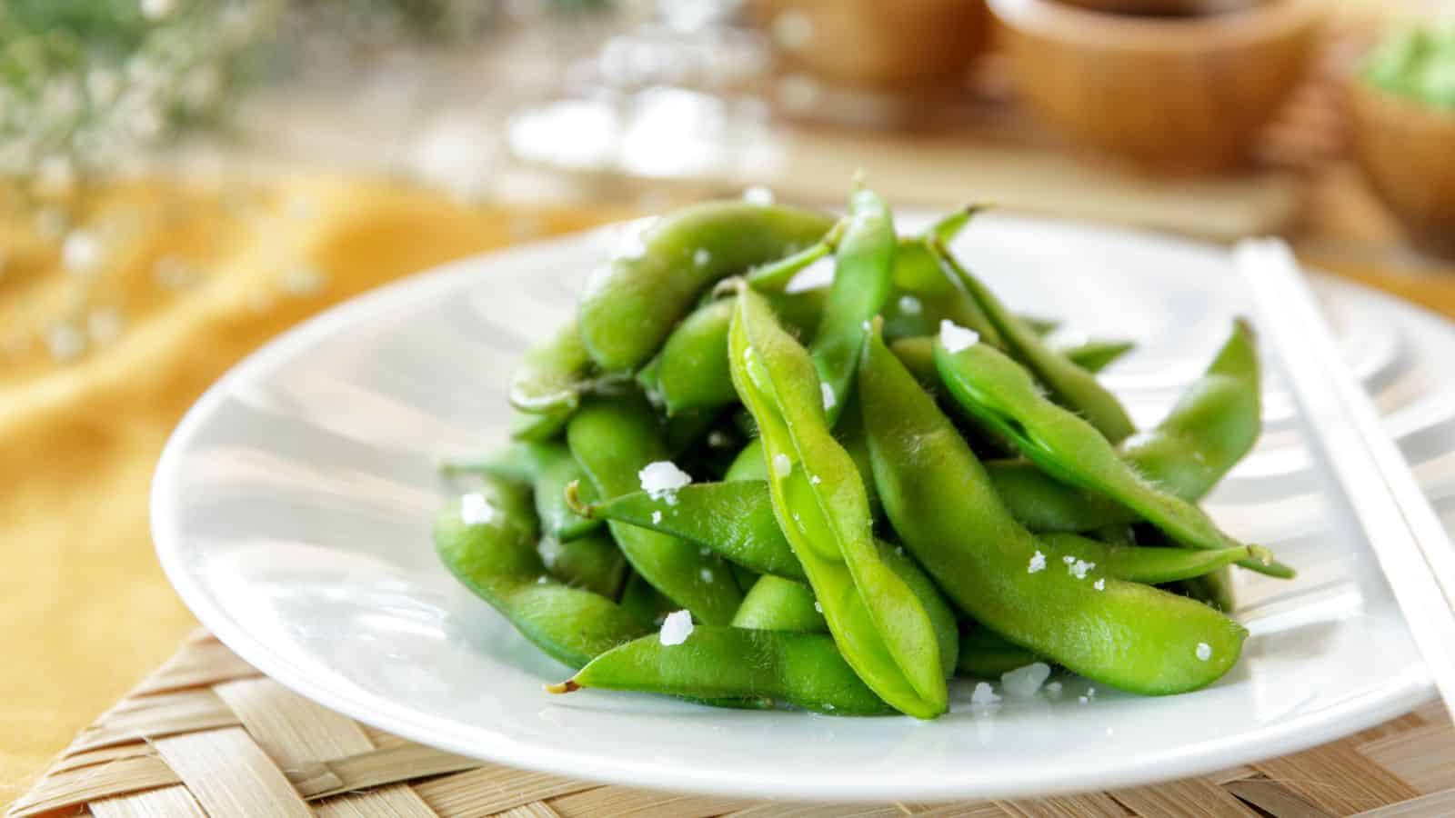 A plate of steamed edamame sprinkled with sea salt on a wooden table, garnished with fresh herbs in the background, showcasing Veggie-Powered Proteins.