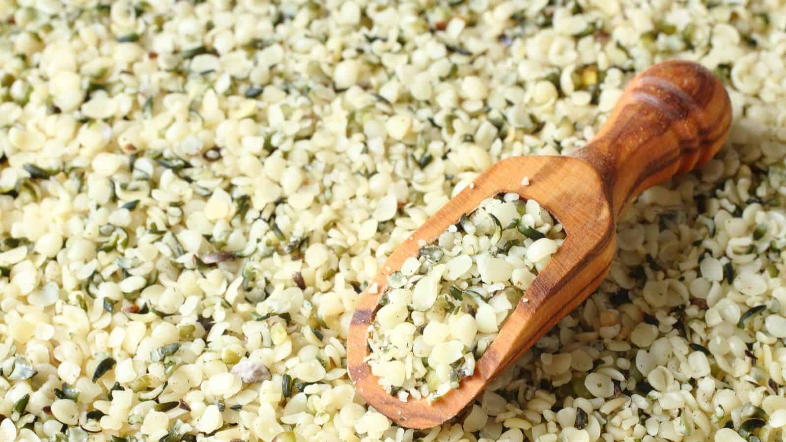 A wooden scoop lying on a pile of chopped garlic mixed with herbs and veggie-powered proteins, filling the frame with its textured, green and white appearance.