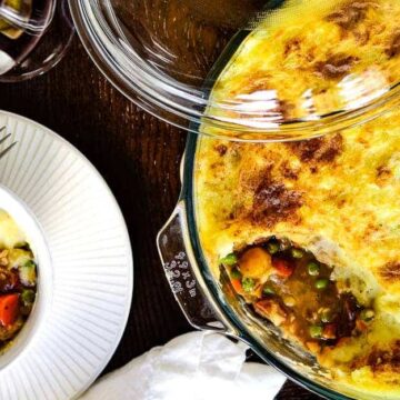 A savory shepherd's pie with a golden-brown mashed potato crust, inspired by Boomers' recipes from the '60s, served on a white plate beside a glass baking dish and a glass of