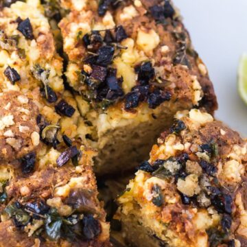 A close-up image of a savory pie topped with crumbled feta cheese and finely chopped black olives, garnished with lime wedges on the side, perfect for Cinco de Mayo recipes.