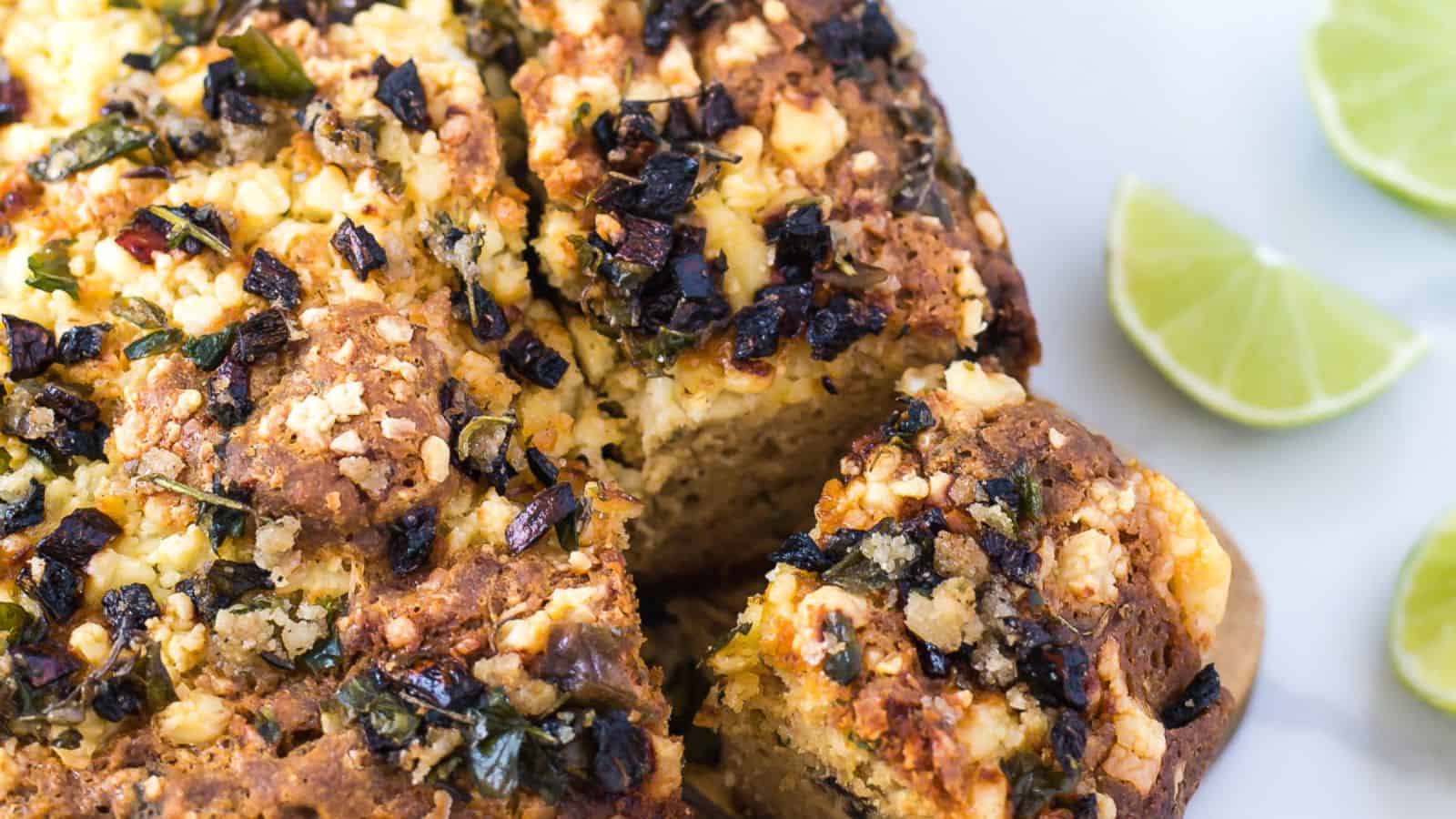 A close-up image of a savory pie topped with crumbled feta cheese and finely chopped black olives, garnished with lime wedges on the side, perfect for Cinco de Mayo recipes.