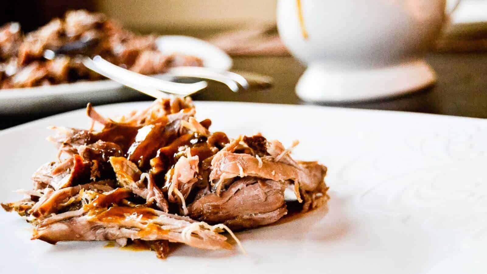 A plate of pulled pork, perfect for a Derby Party, is featured in the foreground with a fork resting on top, set against a blurred background emphasizing the focus on the meal.