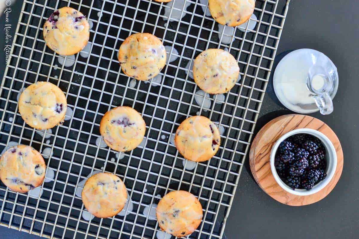 Freshly baked blueberry muffins cooling on a wire rack with a jug of milk and a bowl of blueberries on the side make for an easy breakfast.