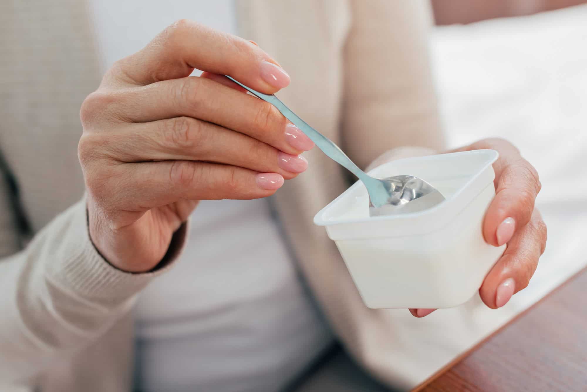 Close-up of a person holding a spoon and a small plastic container of yogurt.