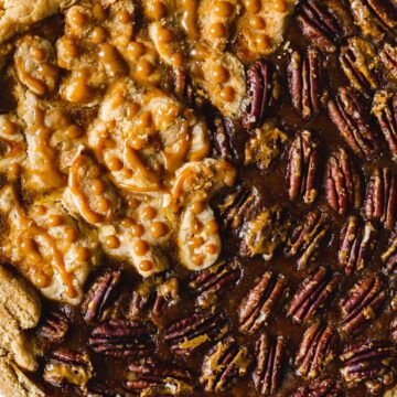 A freshly baked pie with a section of pecans and another of caramelized nuts on a textured cloth backdrop.