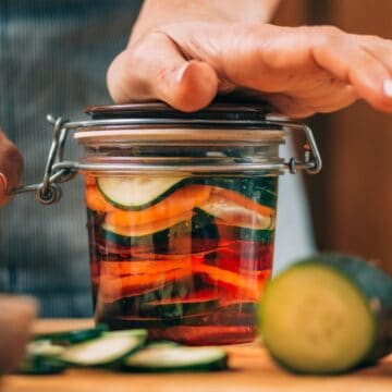 Woman pushing down the lid of a jar filled with cucumbers and carrots
