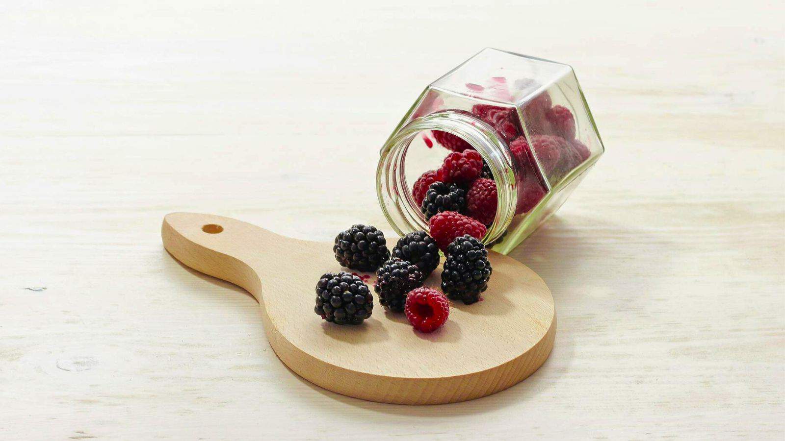 A jar of mixed berries "spilling" onto a board