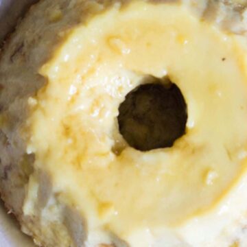 A bundt cake with a yellow glaze is placed in a white bowl. The cake has a circular shape with a hole in the center, and the glaze appears to be evenly distributed across the top. The surface of the cake has a slightly textured appearance.