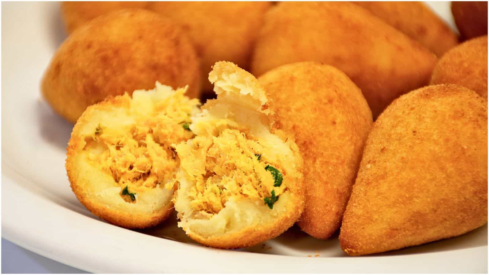 A plate with several golden brown, teardrop-shaped fried pastries, with one cut in half showing a shredded chicken filling mixed with green herbs. These iconic street foods boast a crispy exterior, indicating they are freshly fried.