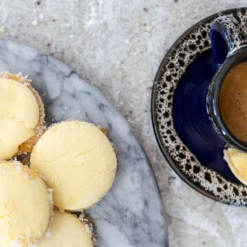 Alfajores cookies filled with dulce de leche and rolled in grated coconut, on a marble plate.