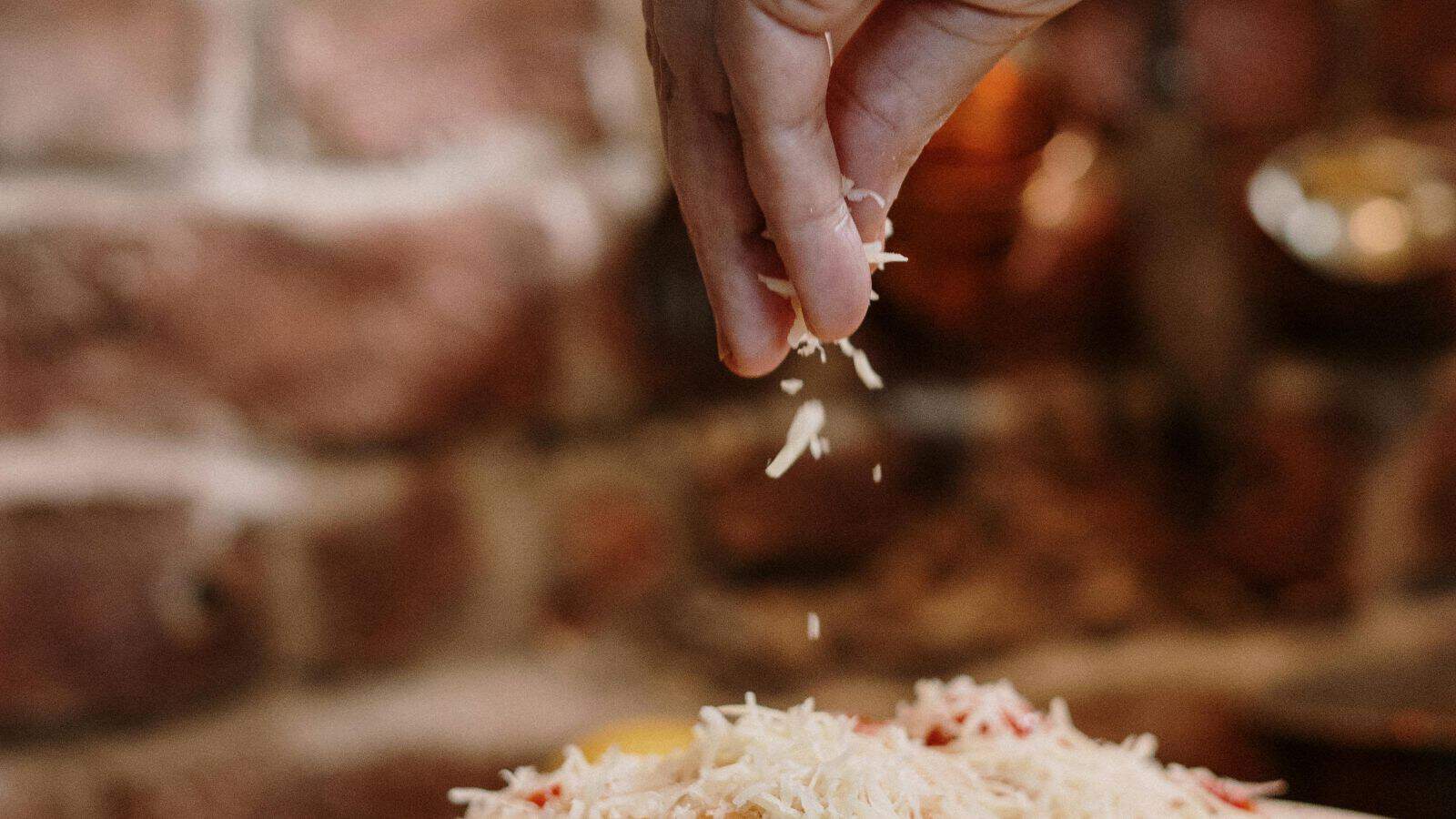 A hand sprinkling grated cheese