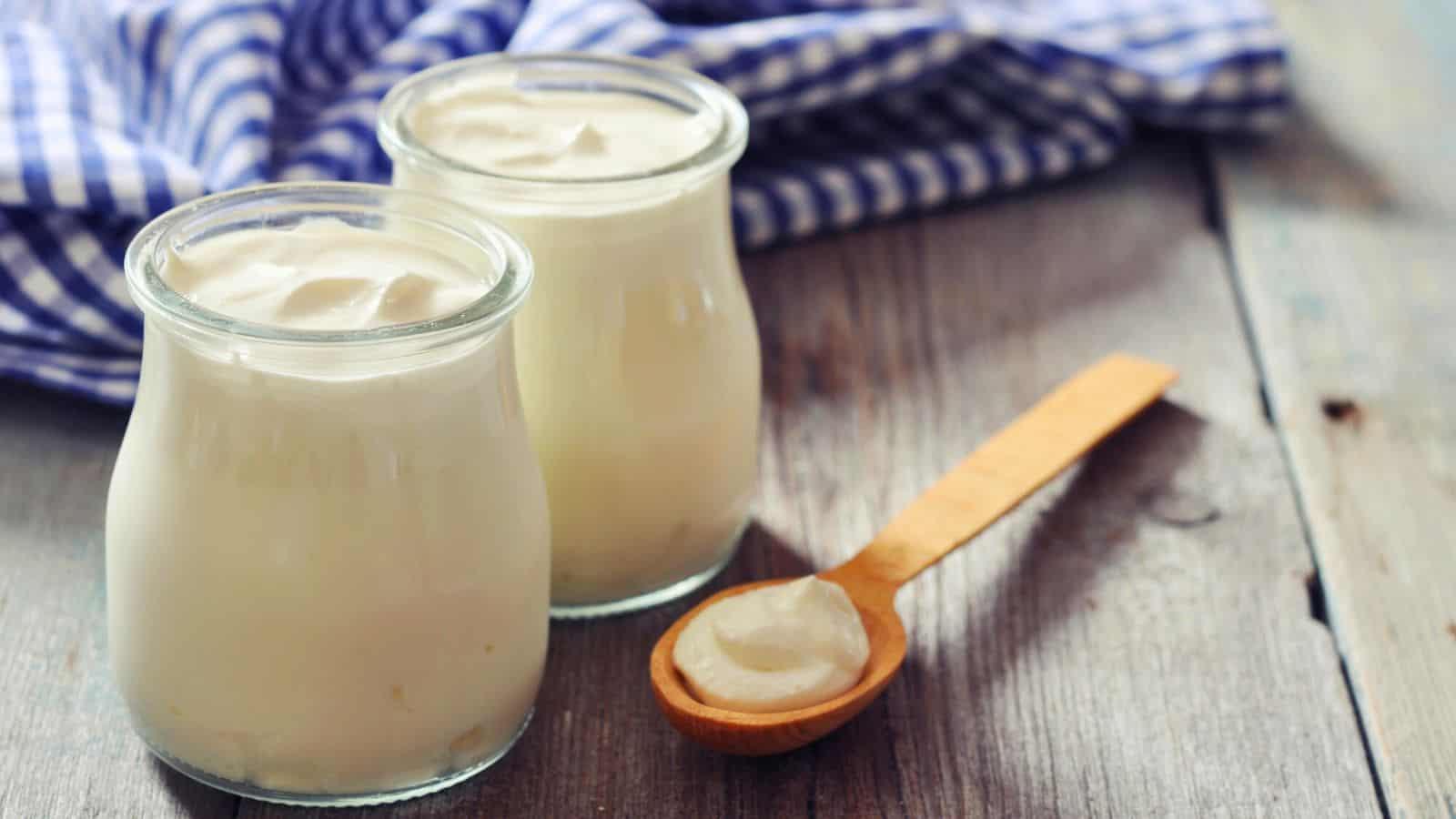 Two jars of Greek yogurt beside a spoon of Greek yogurt 