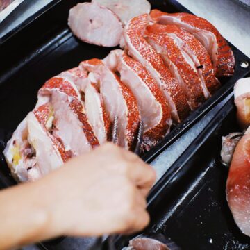 A hand uses tongs to choose from slices of fish
