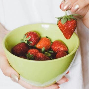 A strawberry plucked from a bowl filled with strawberries