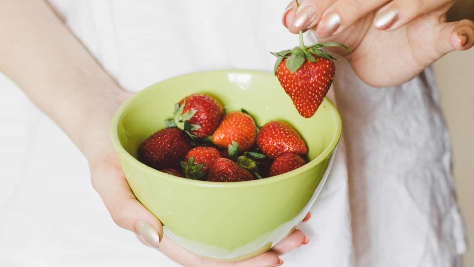 A strawberry plucked from a bowl filled with strawberries