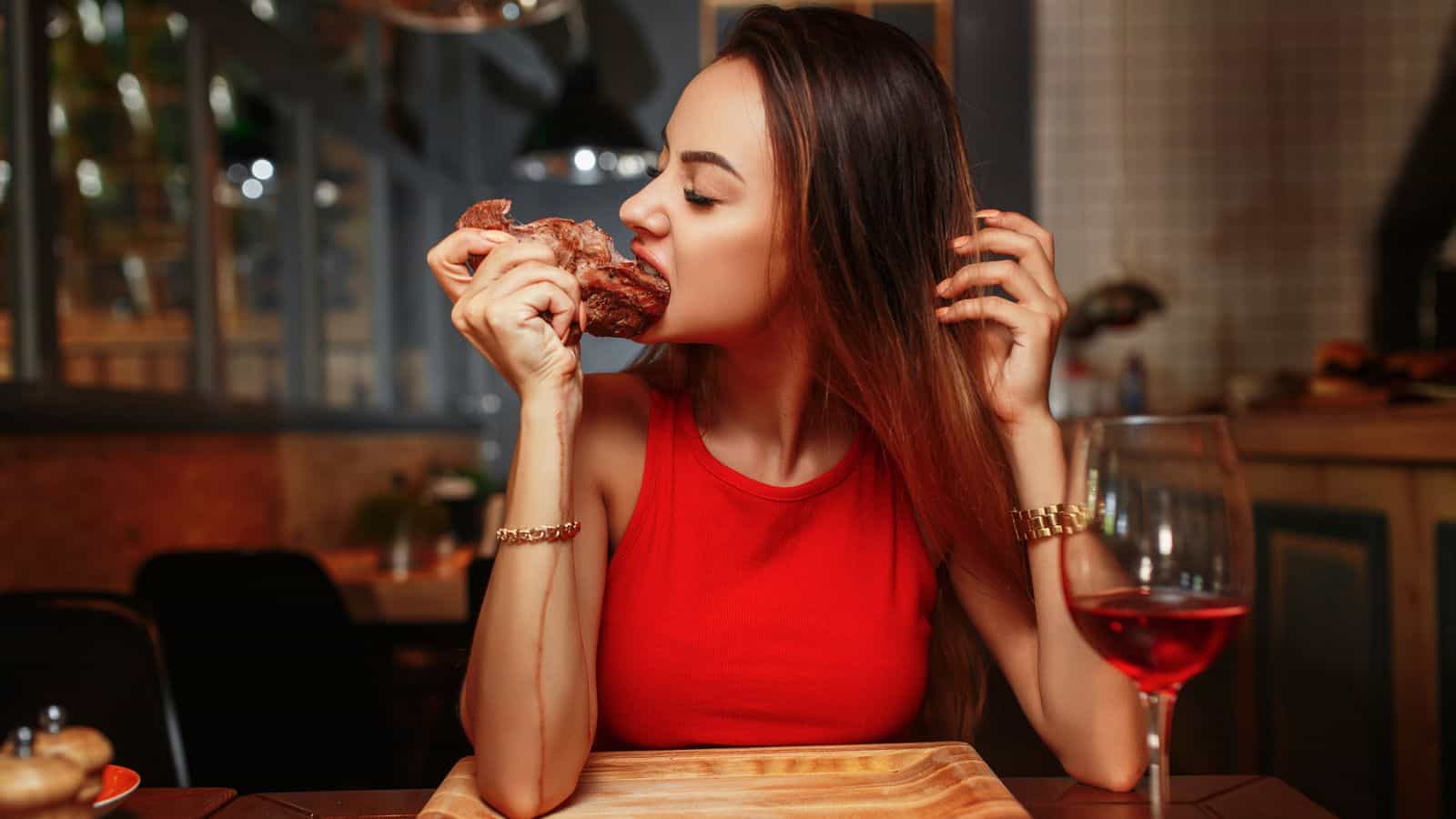 Woman in red dress eating steak by hand