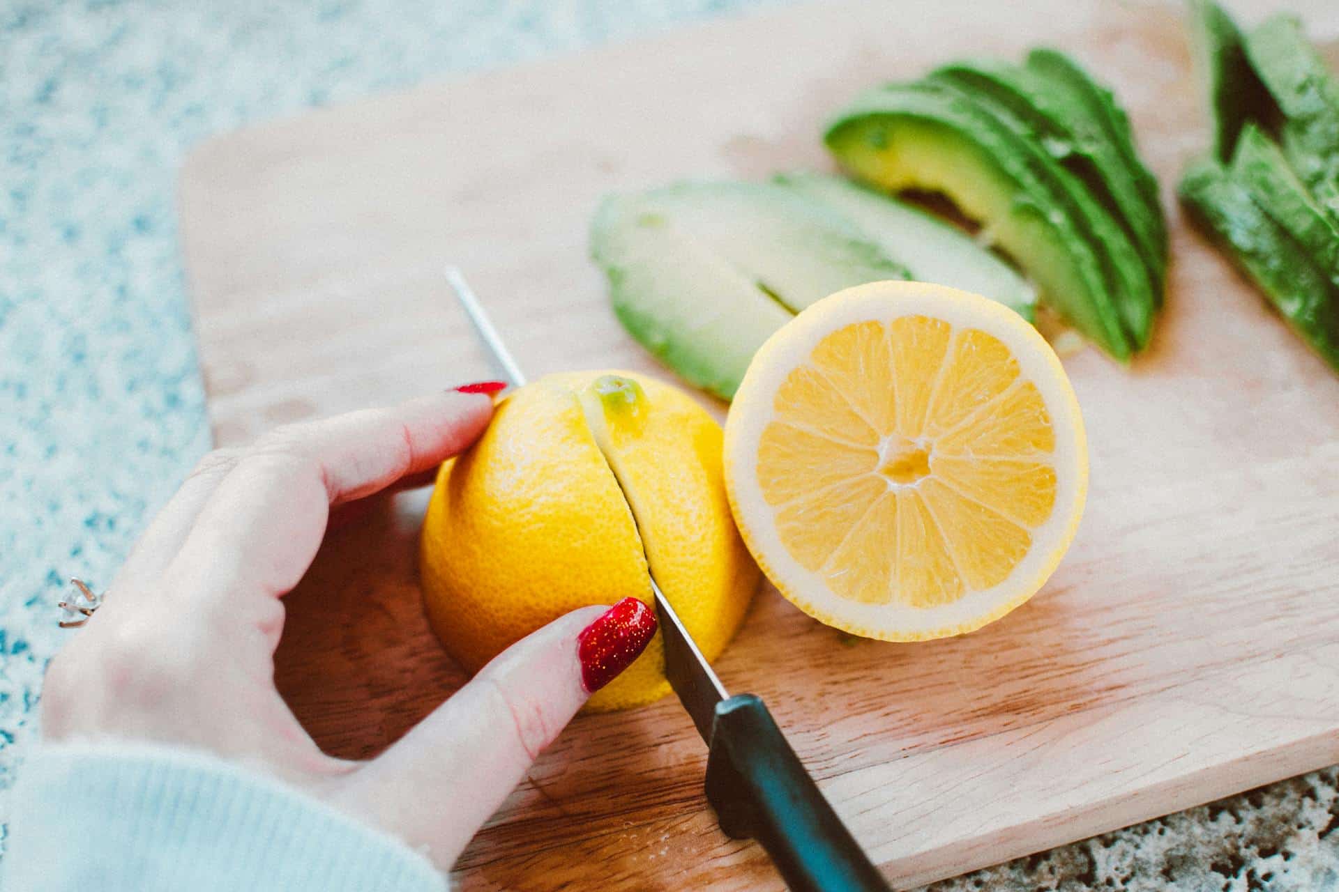A hand slicing a piece of lemon on a chopping board