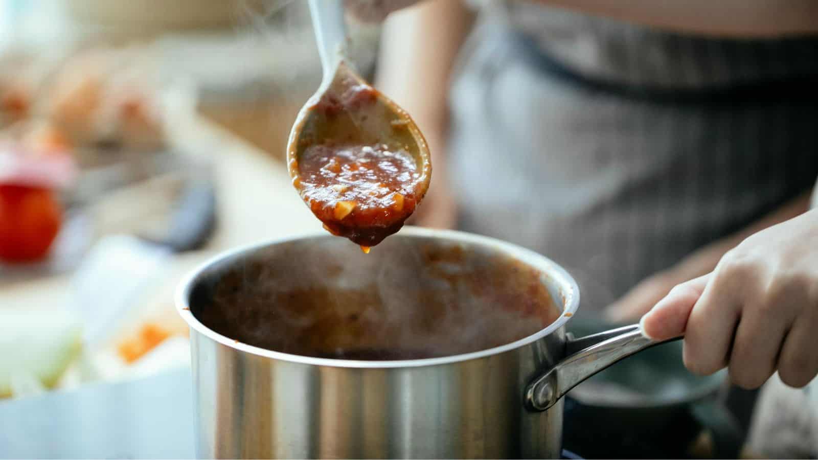 A hand lifting off sauce from a saucepan using a spoon