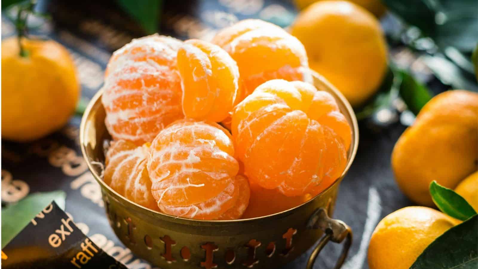 A bowl of peeled oranges with other oranges in the background