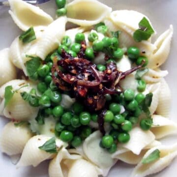 A plate of shell pasta with green peas and caramelized onions, garnished with chopped herbs, makes for one of those easy summer dinners. A fork is partially visible on the plate's edge.