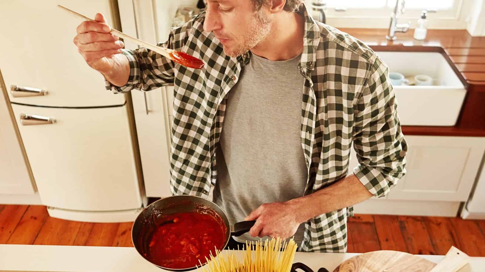 A man tasting spaghetti sauce using a spoon