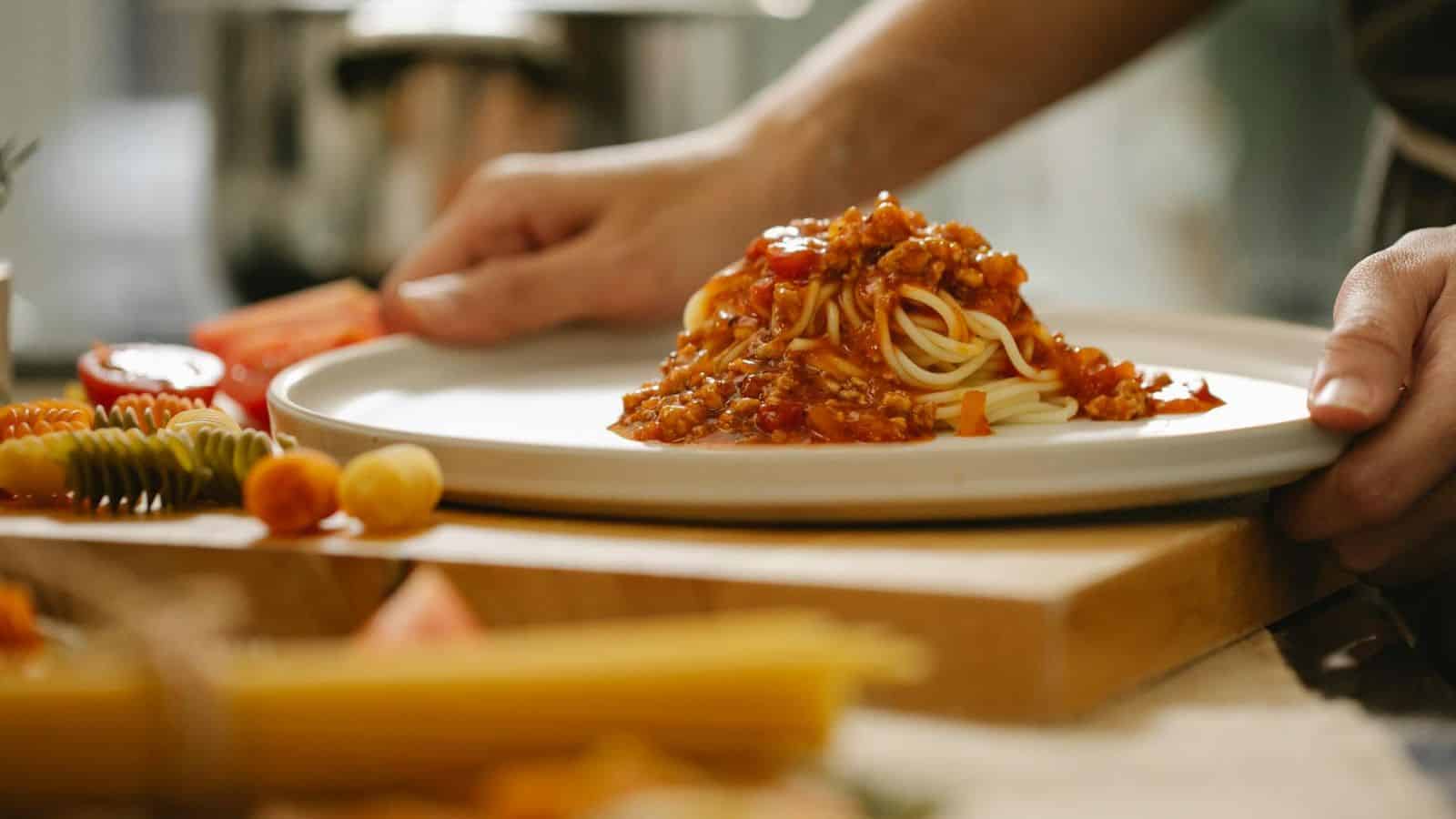 A set of hands holding a plate of spaghetti