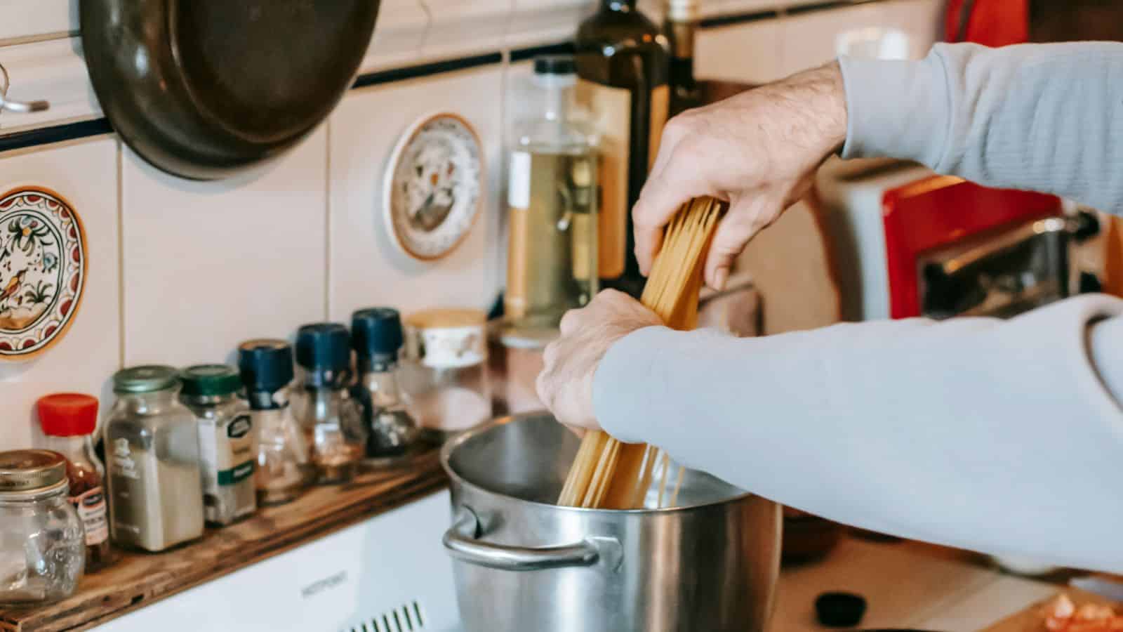 A set of hands putting uncooked pasta into a pan