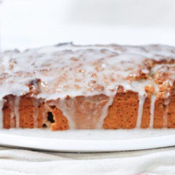 A close-up of a loaf of bread with a white icing glaze on a white plate.