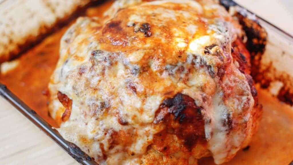 A veggie mains dish featuring a baked cauliflower head in a baking dish with sauce on it.