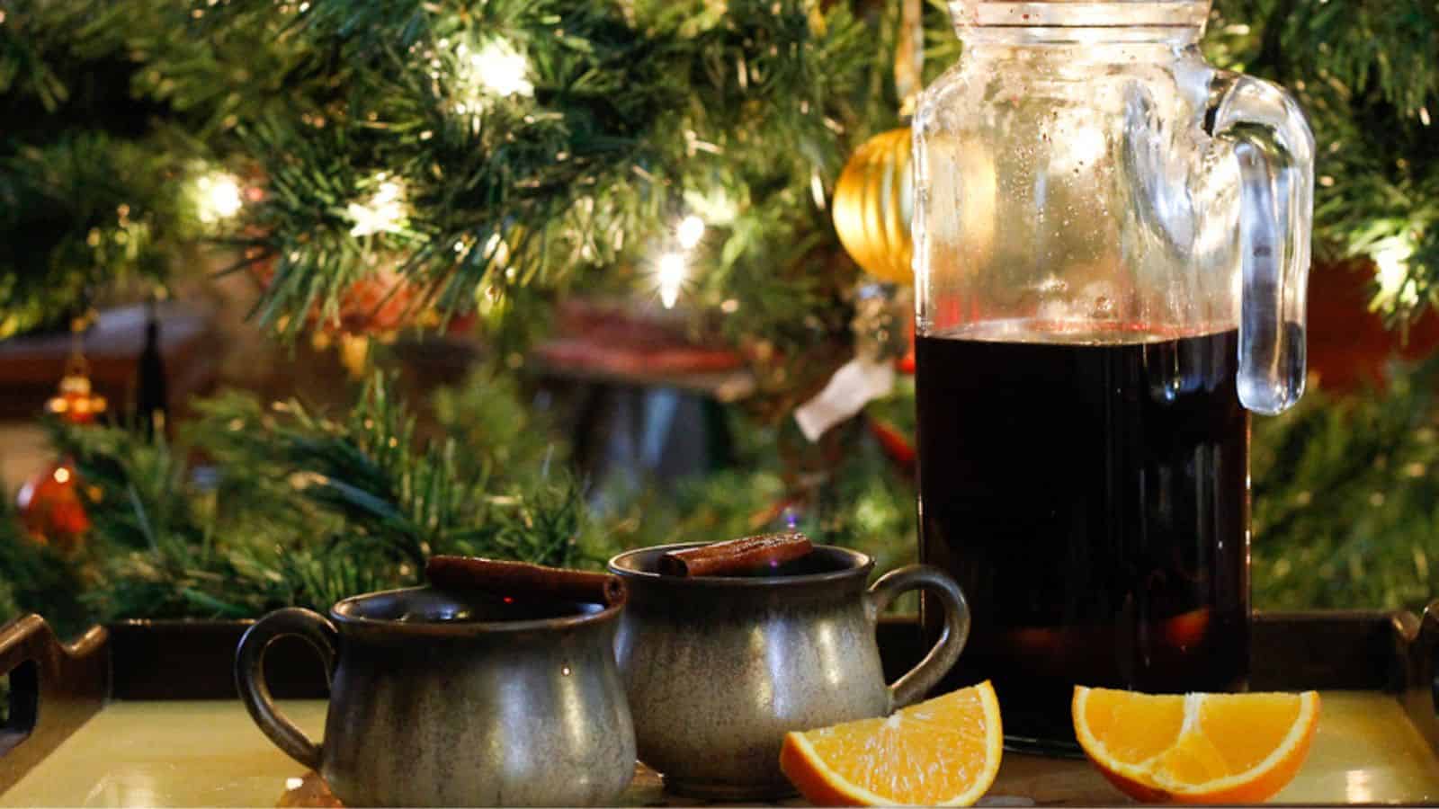 Mulled wine and orange slices on a tray in front of a christmas tree.