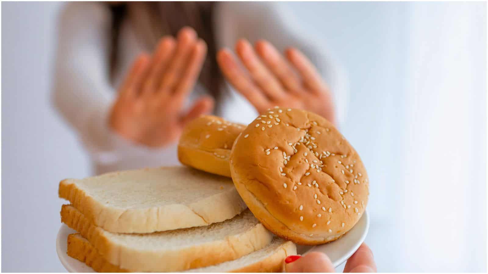 A person is holding up their hands in a stop gesture while being offered a plate with slices of white bread and sesame seed hamburger buns, perhaps signaling a stand against food myths. The background is out of focus, making the gesture and bread the focal point.