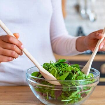 Person mixing a bowl of salad using wooden spoons