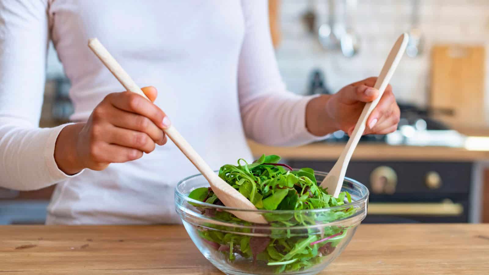 Person mixing a bowl of salad using wooden spoons