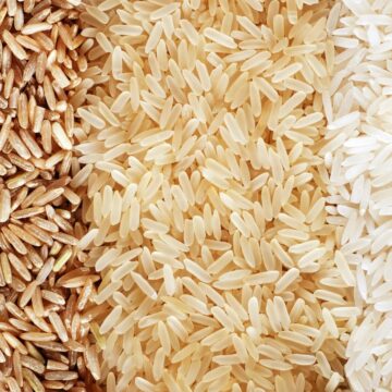 Close-up image of three types of rice. From left to right: brown rice, parboiled rice, and white rice. The grains are neatly arranged in three vertical sections, showcasing their distinct colors and textures.