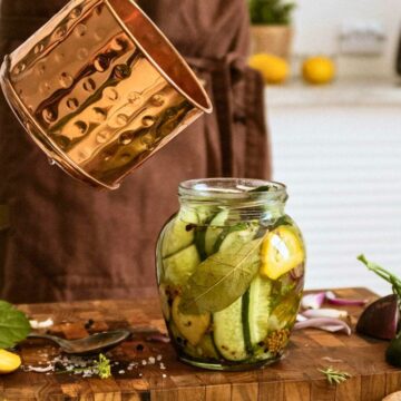 A pot containing what might possibly be vinegar is being poured into a jar full of pickles