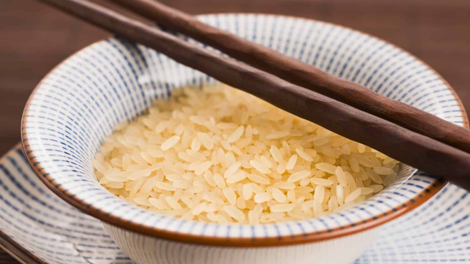 A bowl filled with parboiled rice with a pair of wooden chopsticks resting on top. The bowl is placed on a matching blue and white patterned plate.